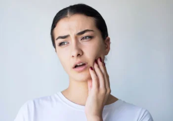 Person holding cheek in discomfort with guidance for relief before visiting Dentist Mustang OK